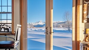 A room with a large window offering a view of snow-covered mountains. - Teton Homestead: Western Cabin w/ Hot Tub & Views (Driggs)