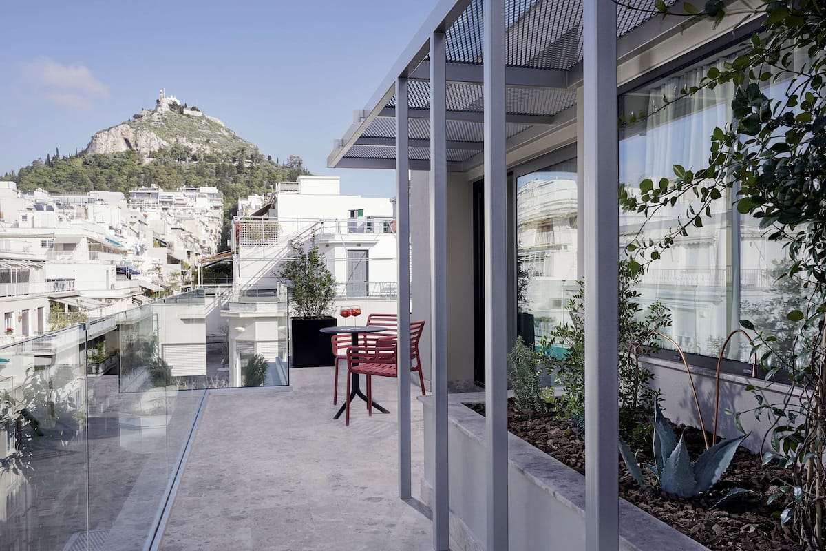 A modern building with a glass balcony overlooking a cityscape and a hill.