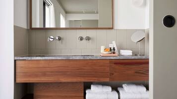 A modern bathroom with a wooden vanity, a large mirror, and neatly folded towels on a shelf.
