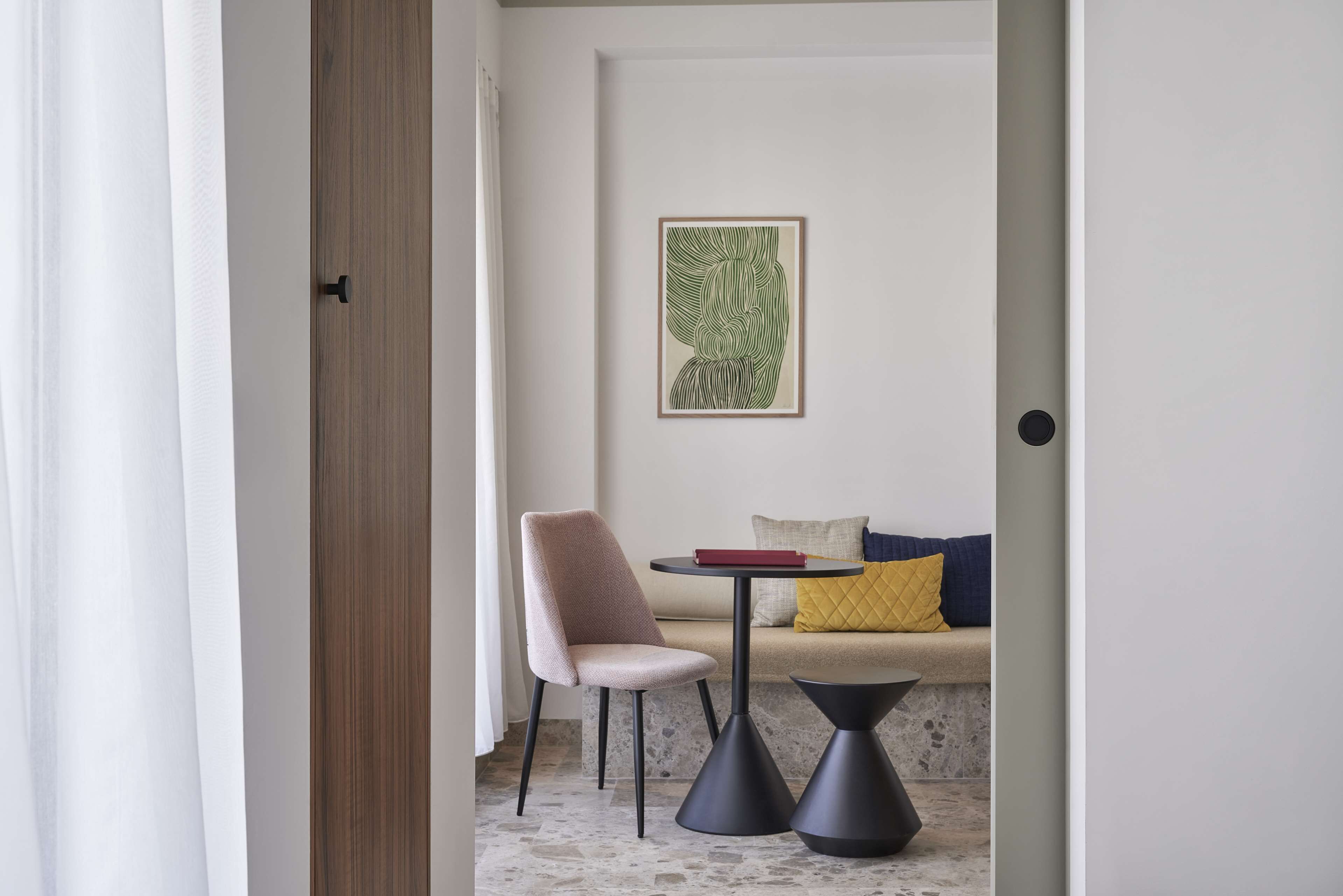 Una habitación moderna con un sofá color beige, una mesita redonda y una silla. Un cuadro enmarcado adorna la pared.