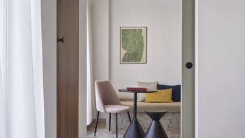 Una habitación moderna con un sofá color beige, una mesita redonda y una silla. Un cuadro enmarcado adorna la pared.