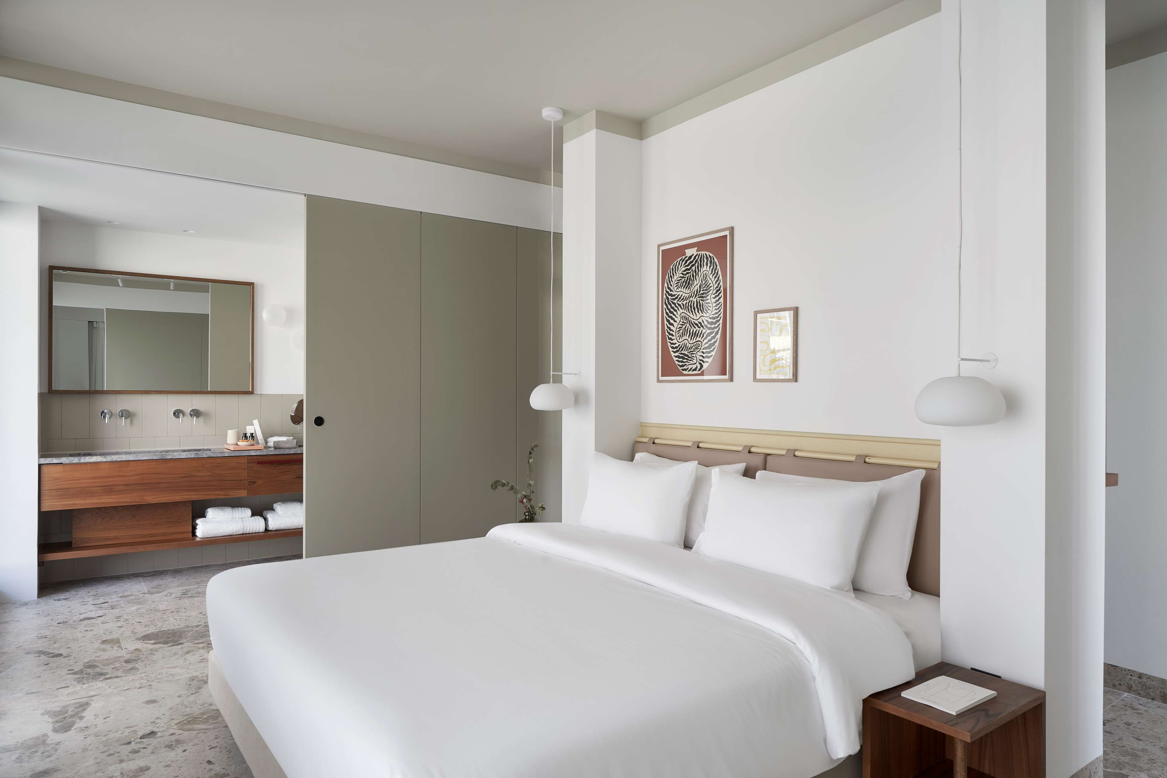 A modern hotel room with a large bed, a wooden vanity with a mirror, and two wall-mounted lamps.