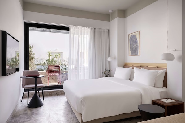 A hotel room with a bed, a small table, a chair, a nightstand, and a window with curtains.