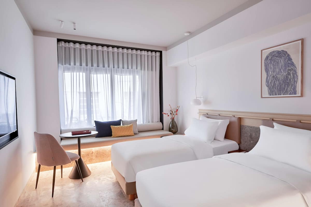 A hotel room with two beds, a sofa, a chair, a small table, and a large window with curtains.