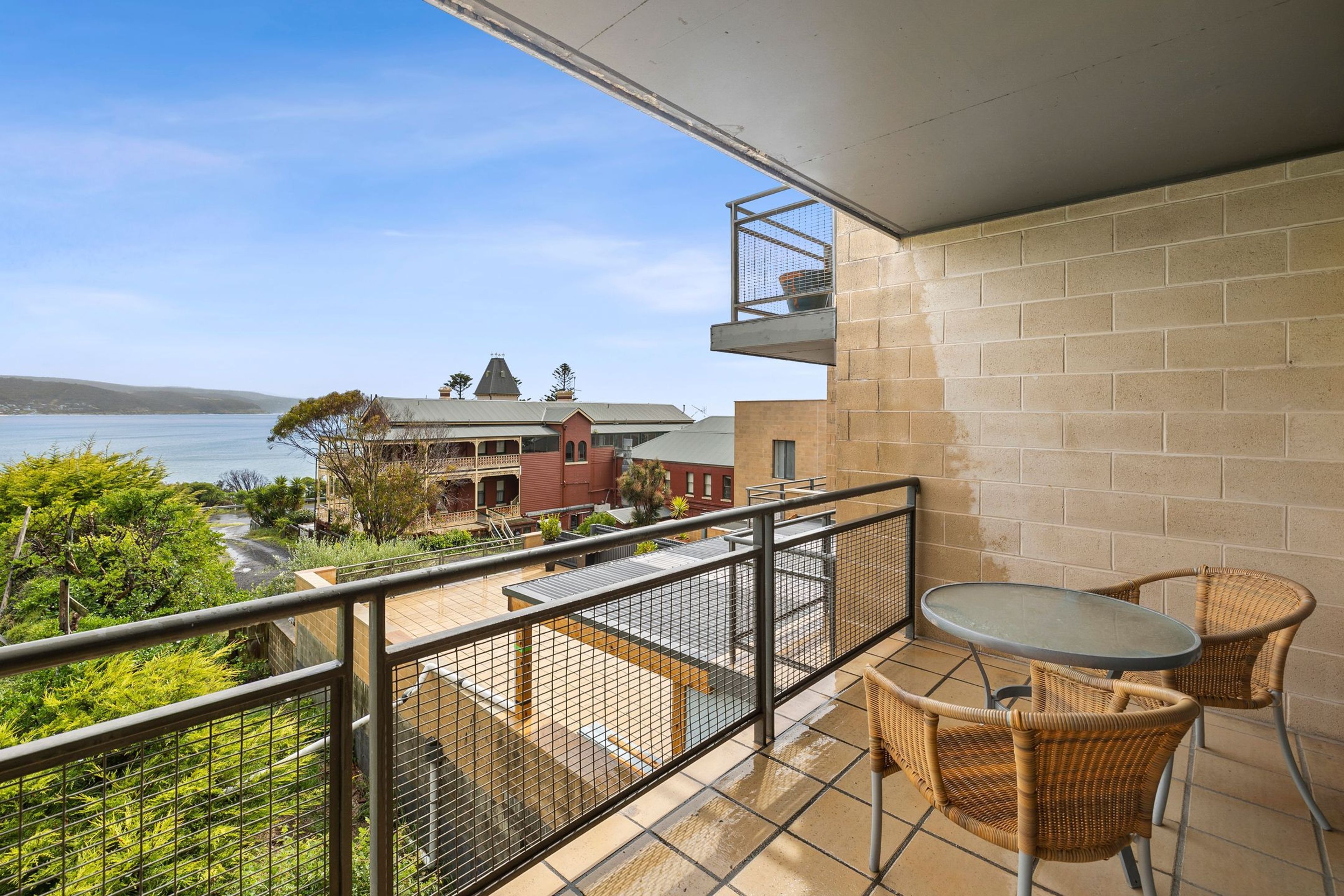 Un balcon avec vue sur la mer, une table et deux chaises en osier.
