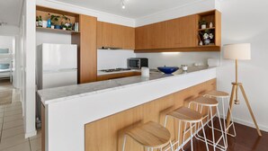 A modern kitchen with wooden cabinets, a white countertop, a built-in microwave, and a blue bowl. - Apartment 30 Pacific Apartments (Lorne)