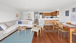 A modern living room with a sofa, coffee table, and dining area with chairs and a wooden table. - Apartment 30 Pacific Apartments (Lorne)
