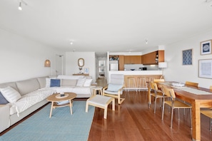 A modern living room with a sofa, coffee table, and dining area with chairs and a wooden table. - Apartment 30 Pacific Apartments (Lorne)