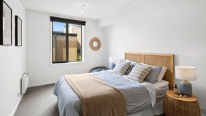 A bedroom with a bed, bedside tables, a window, and a wall-mounted artwork. - Apartment 30 Pacific Apartments (Lorne)