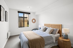 A bedroom with a bed, bedside tables, a window, and a wall-mounted artwork. - Apartment 30 Pacific Apartments (Lorne)