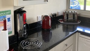 Een keuken met een zwart aanrecht, witte kasten, een rode waterkoker, een broodrooster en een glazen kast.
