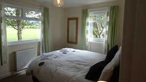 Een slaapkamer met een bed, twee ramen met gordijnen, een radiator en een hanglamp.