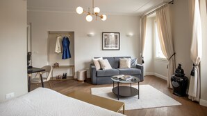 A modern living room with a grey sofa, a round coffee table, and a bed with a patterned duvet. - Daplace - Corso Monforte Suites (Milan)