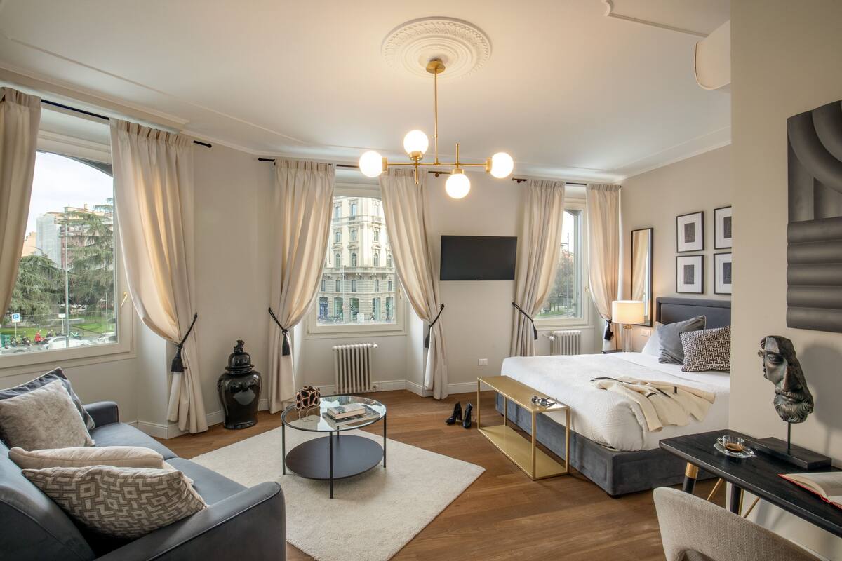 A modern hotel room with a large bed, a sofa, a small round table, and a view of the city.