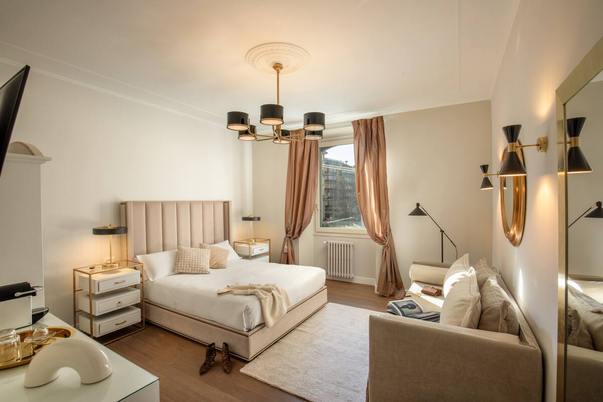 A bedroom with a large bed, bedside tables, a nightstand, a chair, a dresser, a mirror, and a window with curtains.