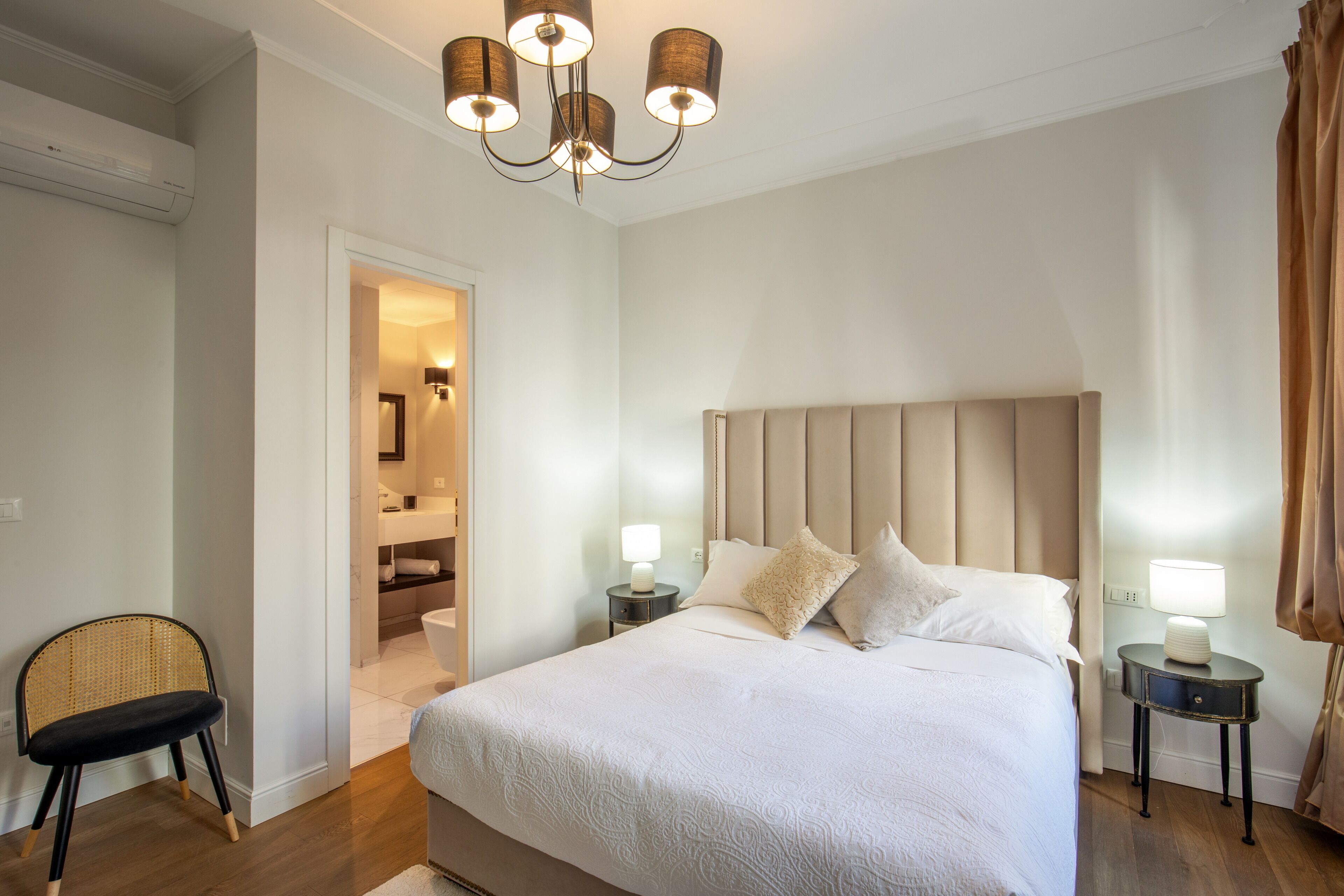 A bedroom with a large bed, bedside tables with lamps, a chair, and a bathroom visible through an open door.