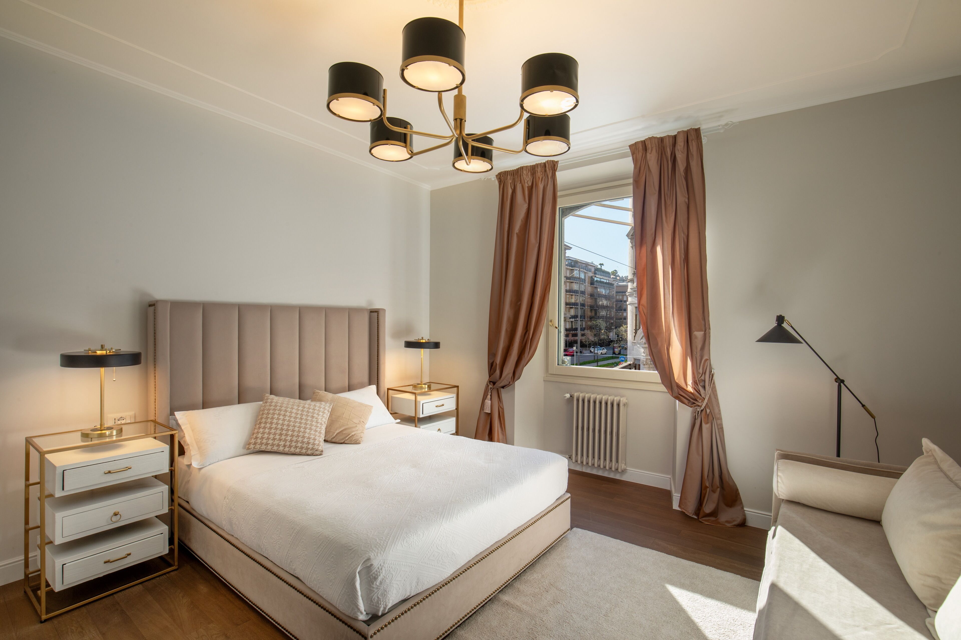 Una camera da letto con un letto grande, comodini, abat-jour e vista sulla città dalla finestra.
