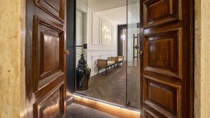 A hallway with wooden doors, a glass partition, and a seating area with chairs and a table. - Daplace - Corso Monforte Suites (Milan)