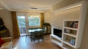 Een woonkamer met een eethoek, een televisie op een witte kast, en een boekenkast.