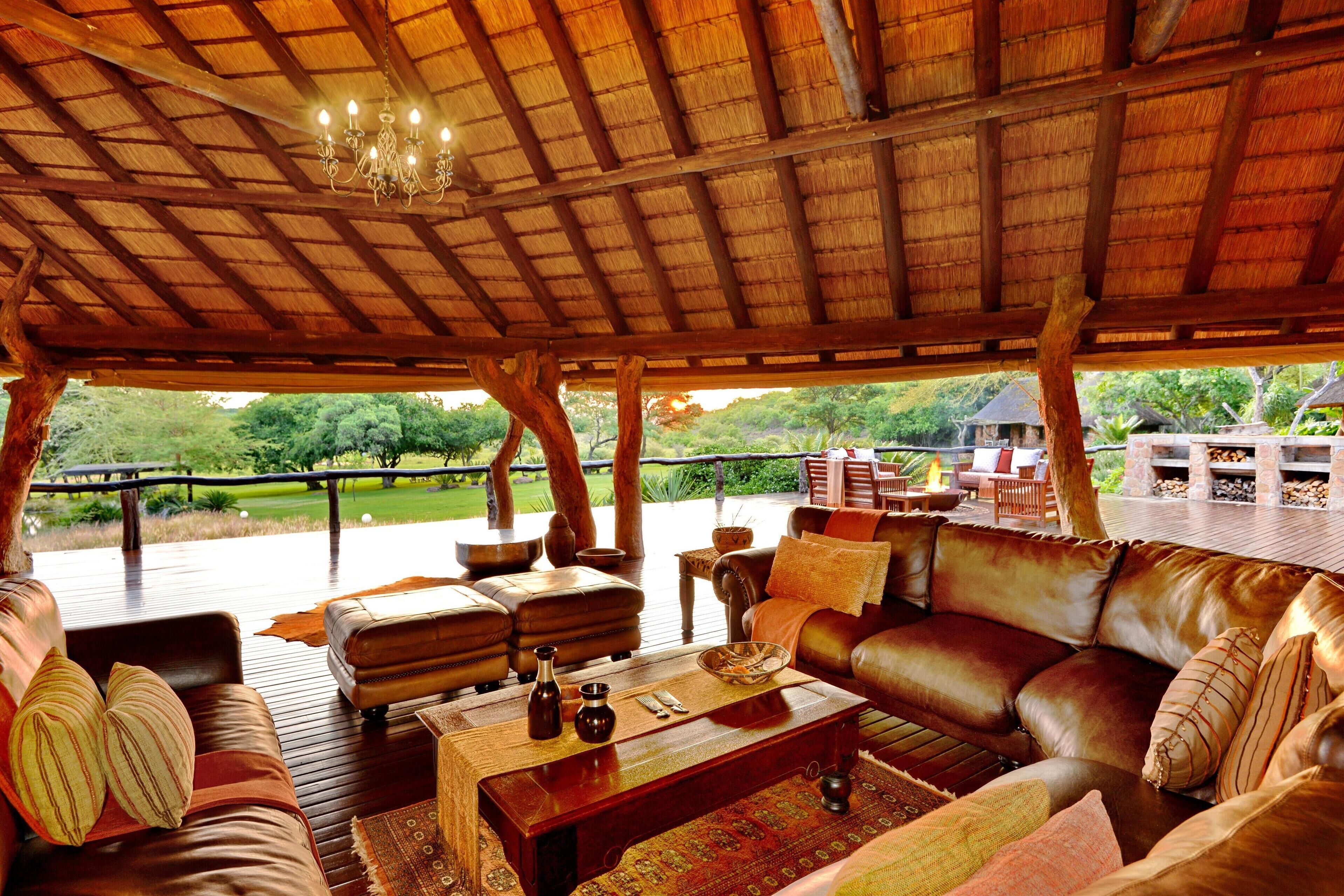 A spacious outdoor seating area with a thatched roof, leather sofas, and a wooden coffee table.