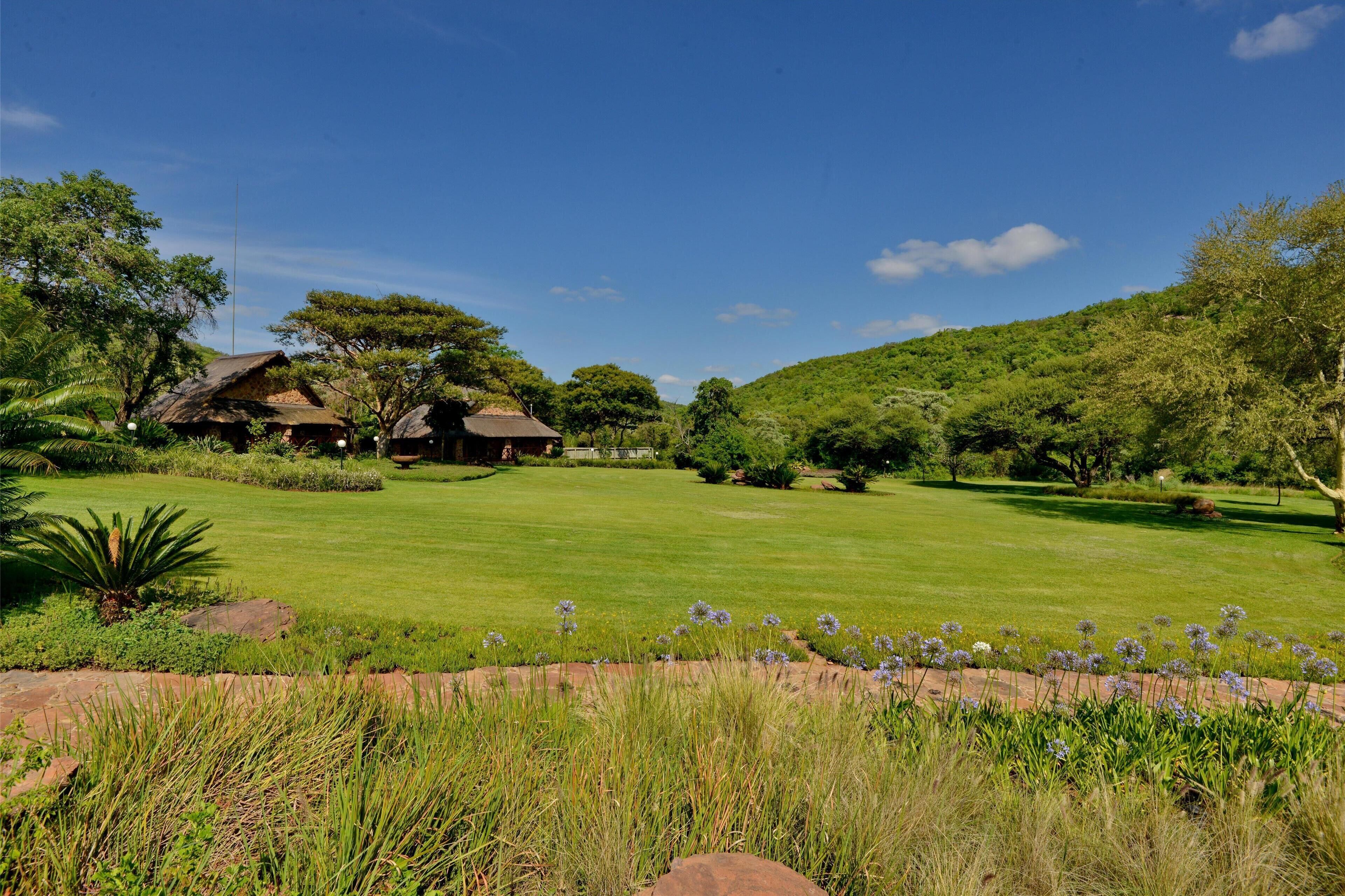 A lush green landscape with a thatched-roof house, surrounded by dense greenery and trees.