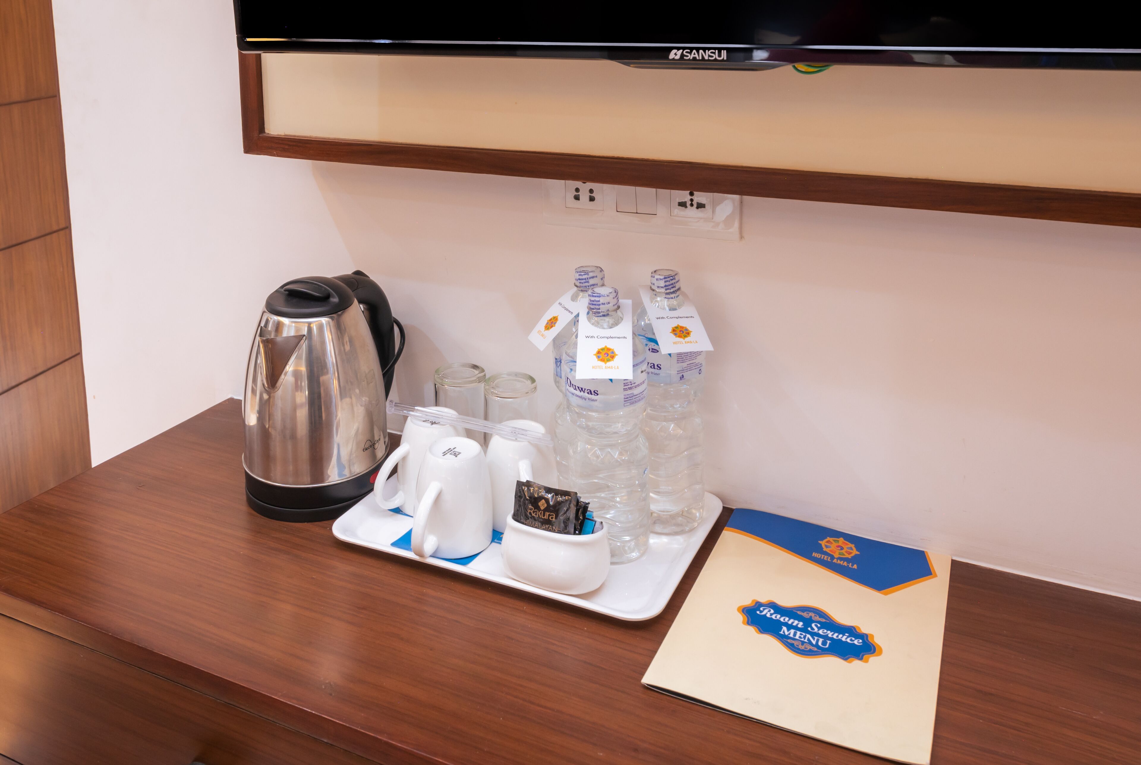 Habitación de hotel con un escritorio de madera, una tetera, tazas, una bandeja con botellas de agua y el menú de servicio a la habitación.