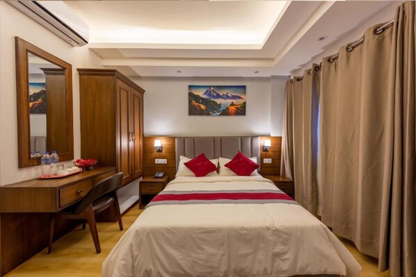 Una habitación de hotel con cama, escritorio, silla, mesita de noche, espejo y un cuadro en la pared.