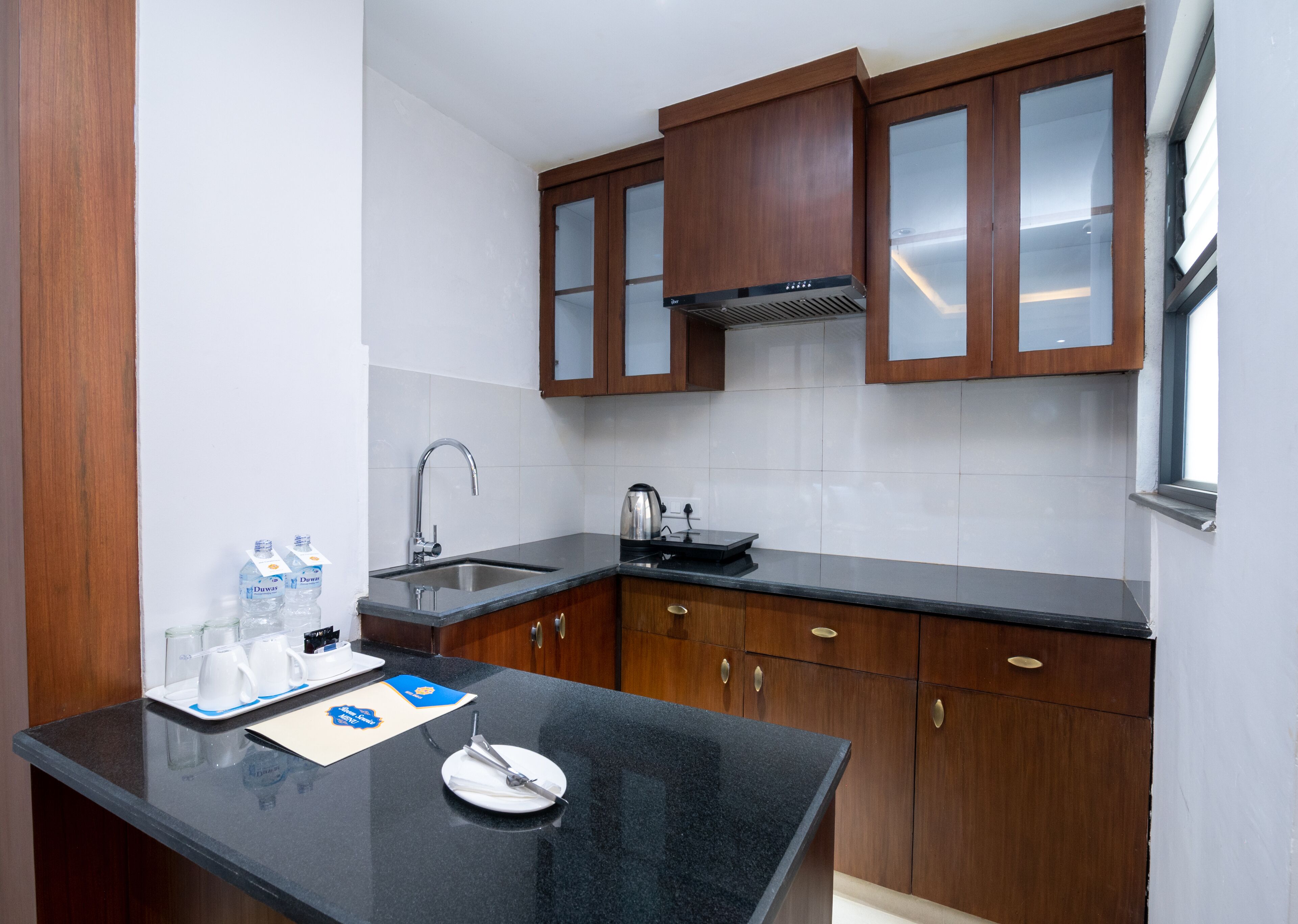 A modern kitchen with wooden cabinets, a black countertop, a stainless steel sink, and a built-in range hood.