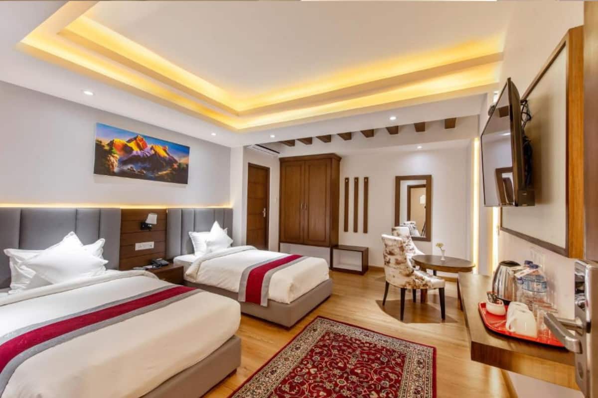 A hotel room with two beds, a desk, a chair, a TV, and a painting on the wall.