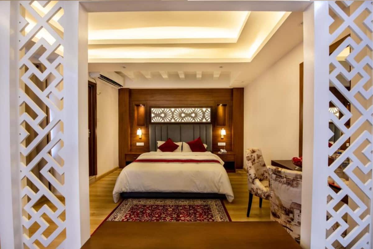 A modern bedroom with a large bed, a decorative headboard, bedside lamps, and a patterned rug.