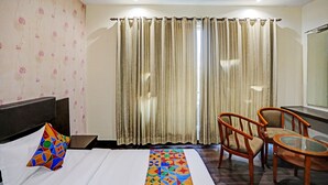 Une chambre d’hôtel avec un lit, une chaise, une petite table et des rideaux.
