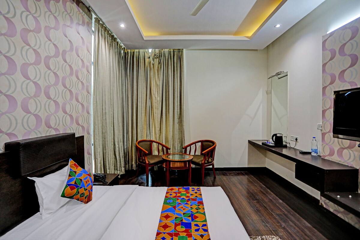 A hotel room with a bed, a desk, a chair, a TV, and a window with curtains.