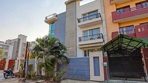Un immeuble résidentiel à plusieurs étages, doté de balcons, d’une entrée sécurisée et de plantes en pot.