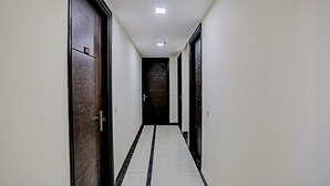 Un couloir étroit, avec des portes en bois foncé et un sol carrelé de carreaux blancs.