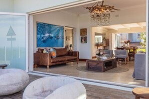 A spacious living area with a large painting, a brown leather sofa, a coffee table, and a view through a glass door.