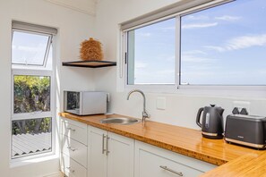 A modern kitchen with a window, a microwave, a sink, and a kettle.