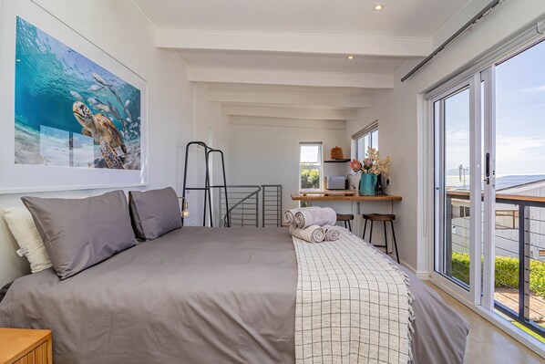 A bedroom with a large bed, a desk with a chair, and a balcony with a view.