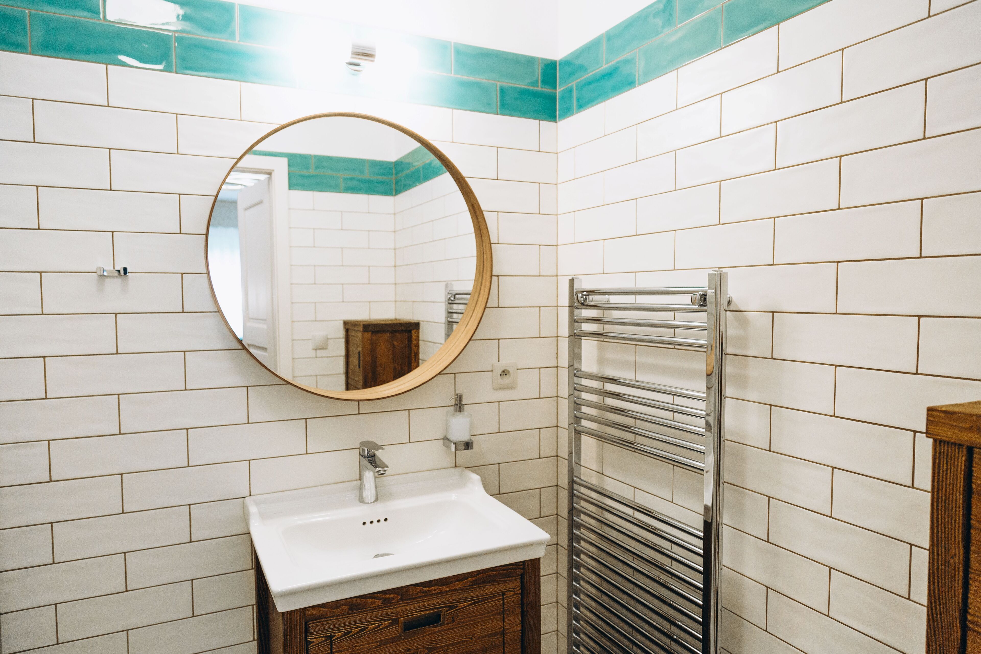 Une salle de bain avec des carreaux de céramique blancs rectangulaires, un meuble-lavabo en bois, un miroir rond et un porte-serviettes.