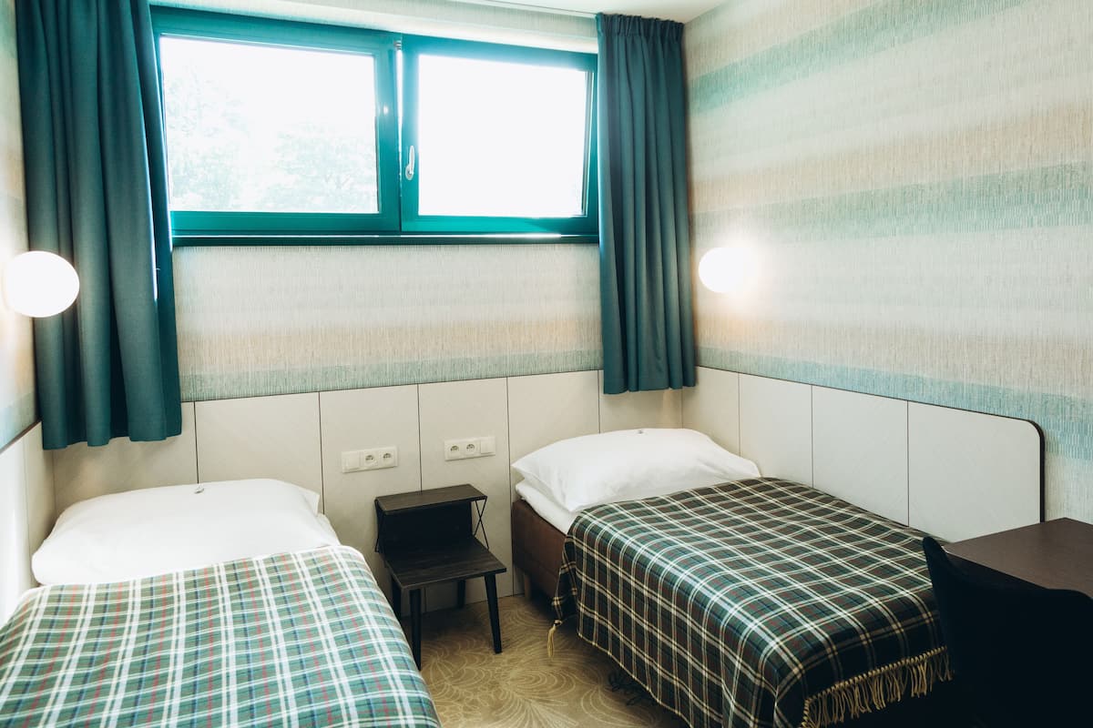 Une chambre avec deux lits, une petite table et une fenêtre avec des rideaux.