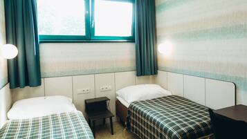A room with two beds, a small table, and a window with curtains.