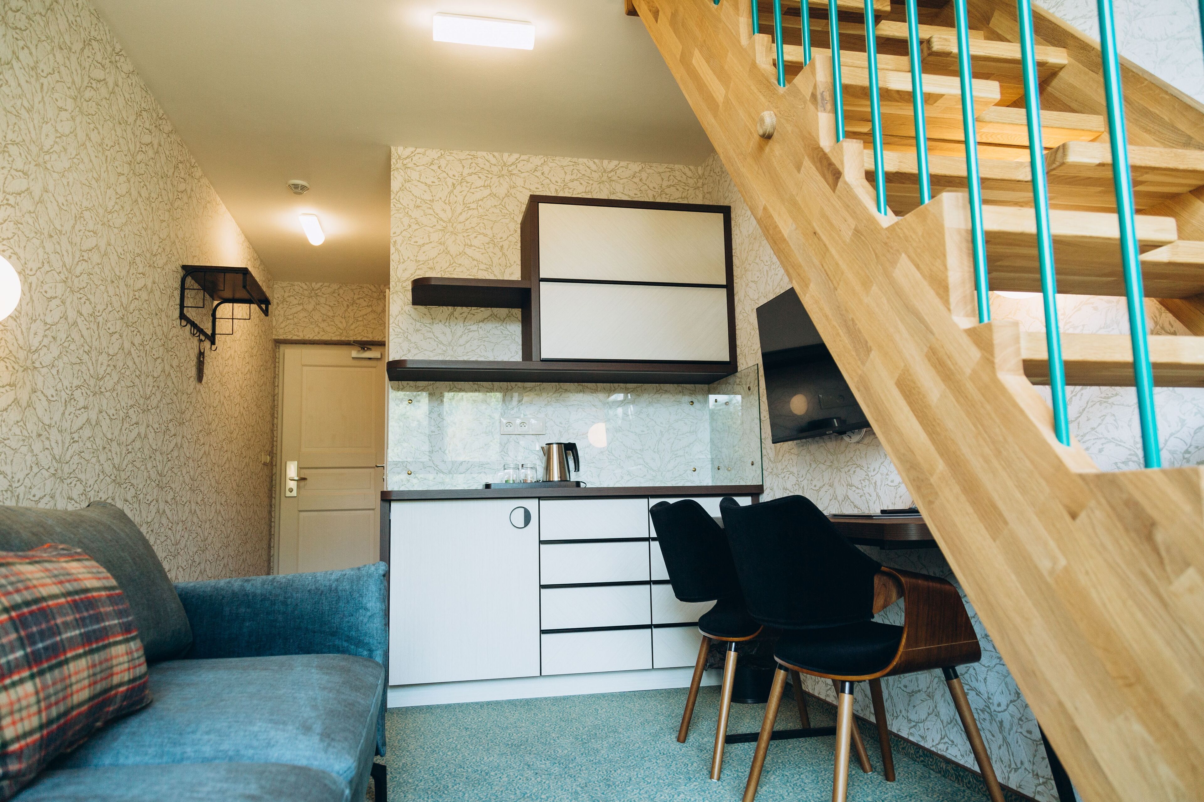 Un espai habitable compacte amb zona de cuina americana, sofà, menjador i escala de fusta.