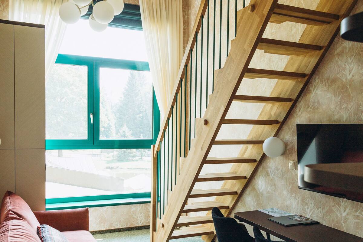 Une pièce avec un escalier en bois, un canapé, une table à manger avec des chaises et un téléviseur fixé au mur.
