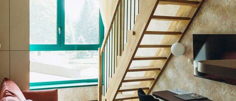 A room with a wooden staircase, a sofa, a dining table with chairs, and a TV mounted on the wall.