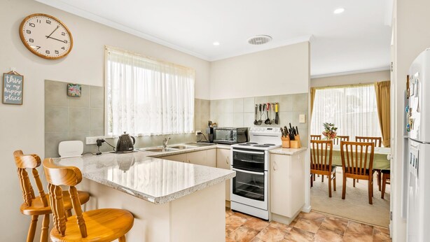 A modern kitchen with a central island, a dining area with wooden chairs, and a refrigerator with magnets. - Cross Rhodes in Wimbledon Heights (Wimbledon Heights)