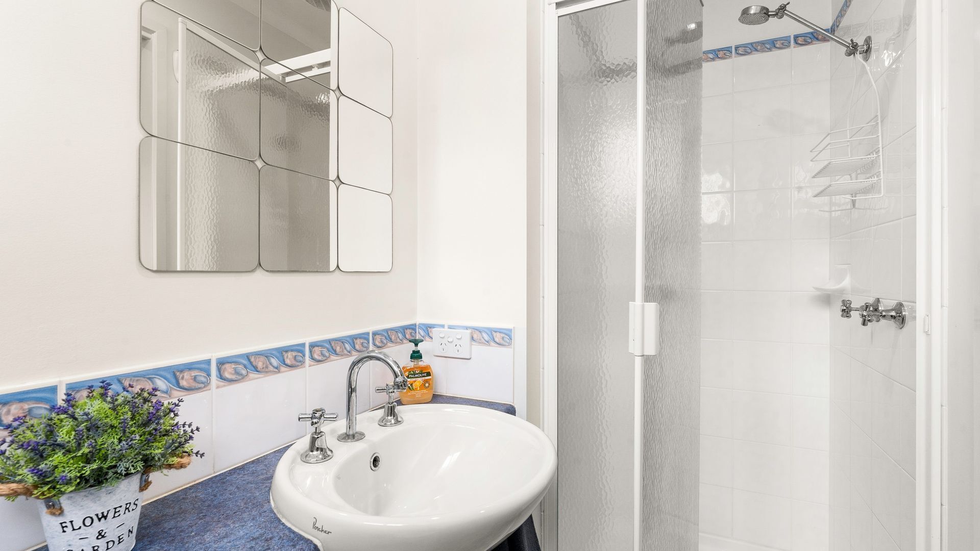 A bathroom with a white sink, a mirror, and a shower with a glass door.