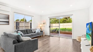 A modern living room with a grey sofa, a lamp, and a large sliding glass door leading to a deck.