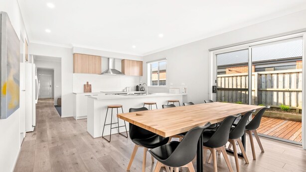 A modern kitchen with a central island, a dining area with a wooden table and black chairs, and a sliding glass door leading to an outdoor patio.