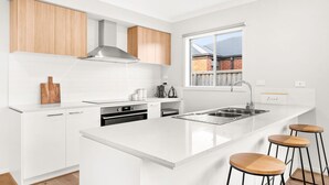 A modern kitchen with white cabinetry, a stainless steel sink, and a large island with bar stools.