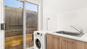 A compact kitchen with a built-in washing machine, a sink, and a sliding glass door leading to a backyard.