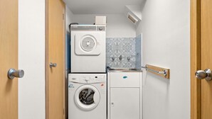 A compact laundry room with a front-loading washing machine, a stacked dryer, and a small sink with a towel rack.